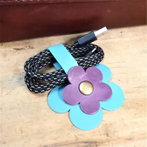 Dettaglio dell'organizer per cavi in pelle a fiore con petali doppi e chiusura a pressione.