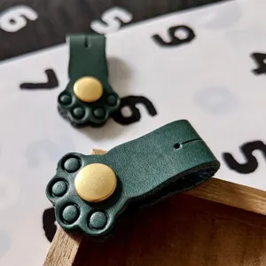 Detailed shot of dark green leather cat paw cable winder with metal snap fastener.
