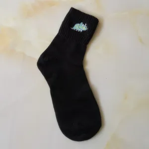 Close-up detail view of the cute blue embroidered dinosaur pattern on the black cotton sock cuff.
