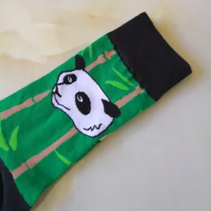 Close-up detail of green cotton crew sock featuring cute cartoon panda and bamboo pattern design.