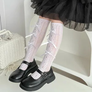 Dettaglio di calze alte in pizzo bianco da bambina con fiocchi decorativi per un look dolce.