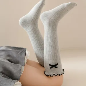 Close-up detail of grey knitted knee-high socks featuring a cute black bow and ruffled edge.