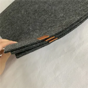 Detalle de mantel de fieltro gris oscuro que muestra textura y lengüeta de cuero.