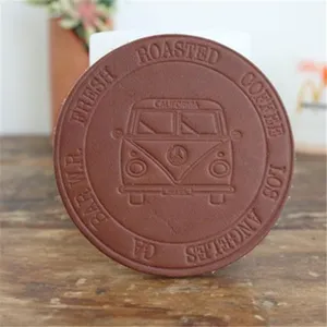 Brauner Lederuntersetzer Detailaufnahme mit geprägtem Retro-Bus-Motiv und Kaffeetext.
