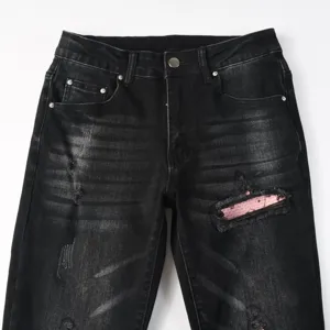 Detailed view of men's black washed distressed denim jeans with pink patch accent.