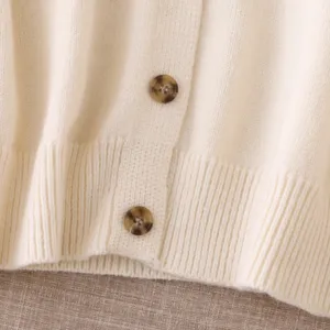 Close-up detail of beige knit cardigan sweater with tortoise buttons and ribbed hem.