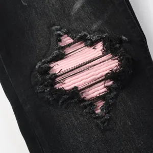 Men's black washed distressed jeans with star shape pink patch detail close up view