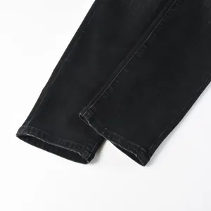 Close-up detail shot of black washed denim jeans cuffs on clean white background.