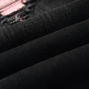 Close-up of black washed denim fabric with pink fleece patch and ripped detail.