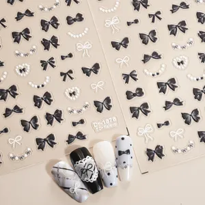 Gedetailleerd overzicht van 5D in reliëf gemaakte zwart-witte strik nagelstickers met elegante parels.