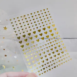 Detailed view of 3D gold foil mini heart nail stickers with adhesive backing on clear sheet.