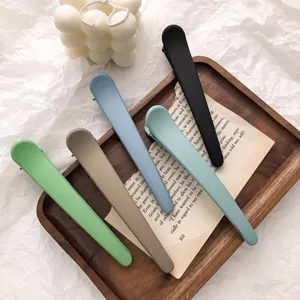 Close-up detail of large matte duckbill hair clips in various colors arranged on a wooden tray.