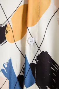 Gros plan sur le tissu de la chemise pour homme avec imprimé abstrait et bouton blanc.