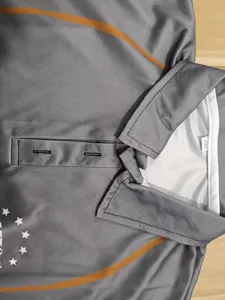 Close-up detail view of grey tactical polo shirt collar with orange stripe and 2XL tag.