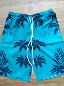 Detail shot of men's summer beach shorts featuring tropical palm leaf print and white drawstring.