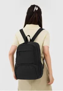 Detailed shot of the classic black backpack worn by a model, featuring practical compartments.