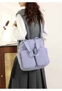 Detail view of the casual multi-pocket nylon crossbody bag in light purple worn by model.
