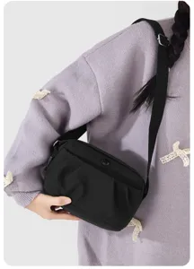 Detailed view of black nylon crossbody shoulder bag, pleated front design with zipper pocket.