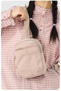 Détail de sac bandoulière en nylon décontracté avec poche avant, sangle large et logo discret.