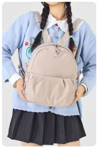 Detailed view of a casual beige small backpack with front pleated pocket and metal logo.