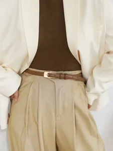 Close-up detail of a minimalist women's thin leather belt styled with high-waisted trousers.