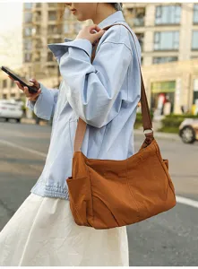 Detailed view of the large capacity nylon shoulder bag in brown, worn casually in a street setting.