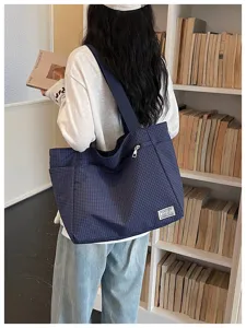 Vue détaillée du sac cabas fourre-tout à carreaux bleus devant une bibliothèque.