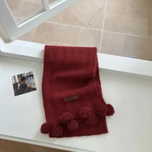 Vue détaillée de l'écharpe en tricot rouge foncé avec des pompons mignons et une texture douce.