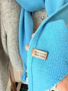 Gros plan détaillé d'une écharpe en laine bleue douce avec des franges et une étiquette.