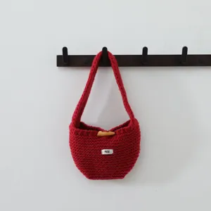 Détail de sac à main en tricot rouge avec fermeture à bouton en bois et petite étiquette.