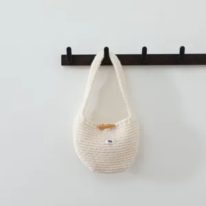 Sac à main en laine tricotée, vue de détail, texture douce, bouton et étiquette.