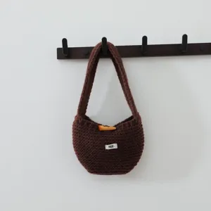 Sac à main en tricot marron avec bouton en bois et petite étiquette tissée pour les femmes.