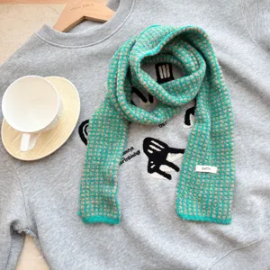 Vue détaillée d'une longue écharpe fine en tricot à carreaux vert et marron texture douce