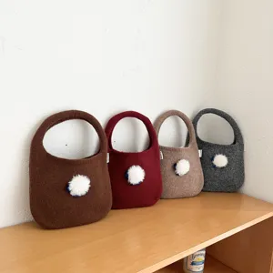 Vue détaillée de sacs à main en tricot mignons avec pompons duveteux présentés sur une étagère.