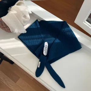 Détail de foulard triangulaire en tricot bleu foncé, montrant la texture ajourée et les liens.