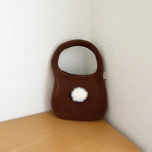 Sac à main en tricot marron douillet avec pompon blanc, fourre-tout tendance automne hiver.