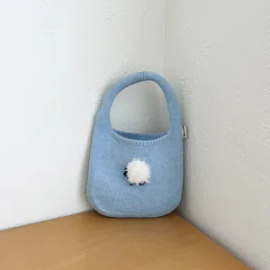 Vue détail d'un sac à main en tricot bleu clair avec un charmant pompon duveteux.
