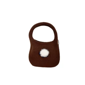 Sac à main en tricot marron avec joli pompon blanc duveteux, design élégant et compact.