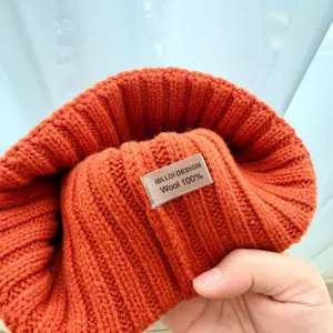 Gros plan du bonnet en tricot 100% laine orange, montrant une texture confortable et une étiquette.