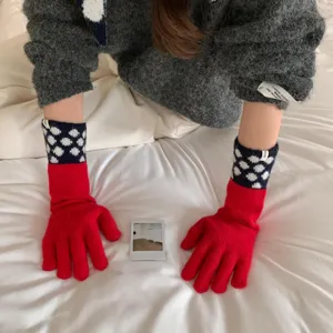 Gros plan détaillé de longs gants en tricot rouge avec poignets à pois sur le lit.
