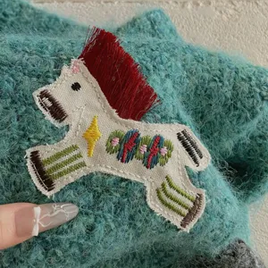 Close-up detail of knitted mohair scarf with colorful horse embroidery patch and fringe.