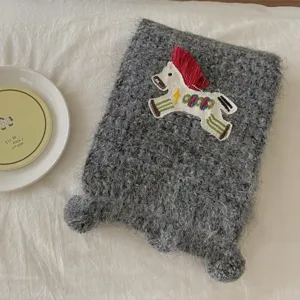 Closeup of grey fluffy knitted scarf featuring cute embroidered horse patch and cozy texture.