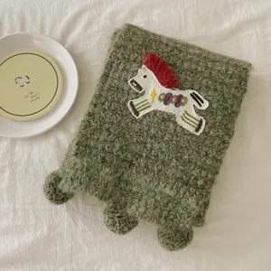 Cozy green knit scarf detail showing cute embroidered horse patch and fuzzy texture design.