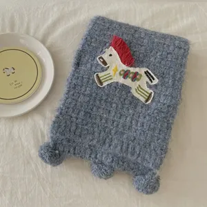 Cozy blue knit winter scarf detailed with cute horse embroidery and sweet pom pom ends.