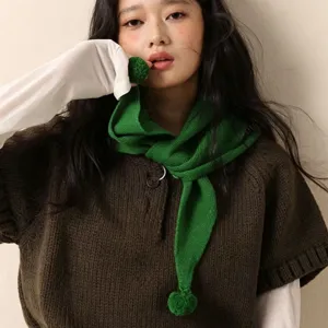 Vue détaillée d'écharpe triangulaire en tricot vert avec pompons, accessoire d'automne hiver.