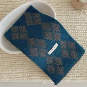 Gros plan sur une douce echarpe en tricot argyle bleu gris avec une etiquette effet laine.