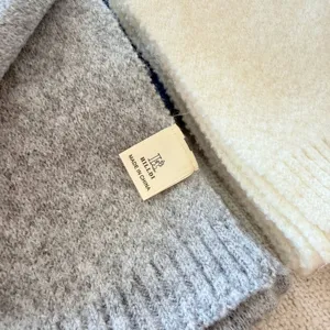 Close-up detail van de zachte wolmix gebreide sjaal stofstructuur met duidelijke merklabel.