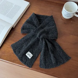 Detailed view of dark grey wool blend cable knit scarf with brand label on wooden table.
