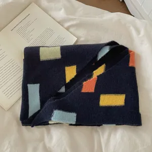 Vue détaillée d'une écharpe en tricot douillette avec des blocs géométriques colorés foncés.