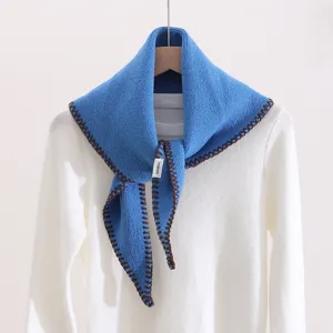 Blue knitted triangular scarf detail showing the unique brown edge stitching and soft texture.